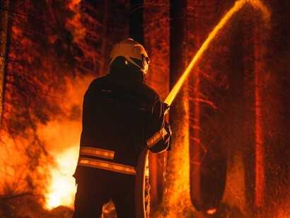 A firefighter using a high-pressure hose to battle a large and dangerous forest fire