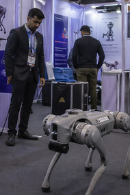 A robotics demonstration at a crowded technology exhibition, where a quadruped robot and surrounding displays highlight the fine line between innovation, presentation, and perception in modern AI showcases