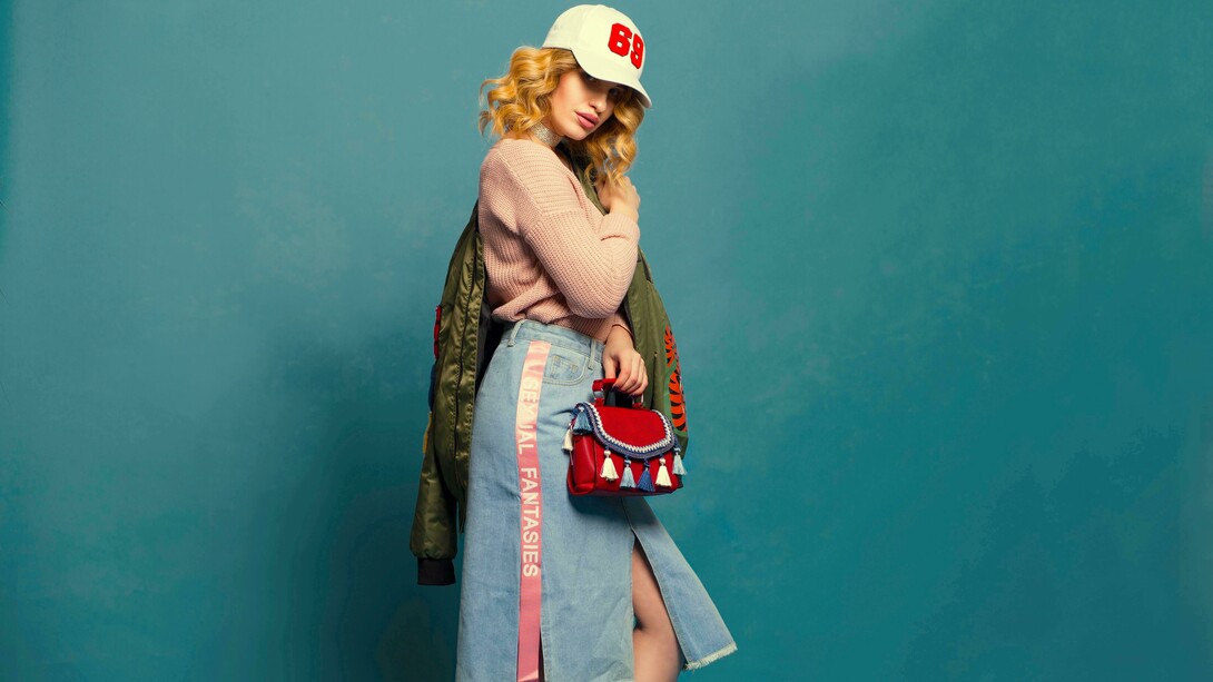 Foto de mulher vestindo saia jeans, agasalho de lã com uma jaqueta verde musgo e um boné branco