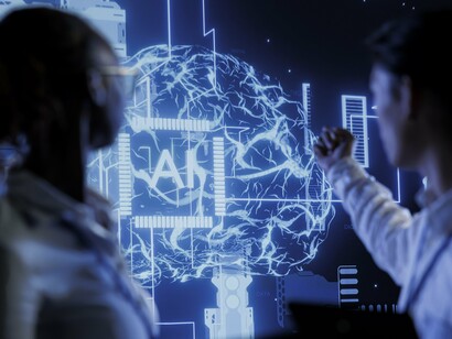 A person gestures toward a neural network display as their colleague observes, reflecting the human role in guiding AI toward meaningful innovation
