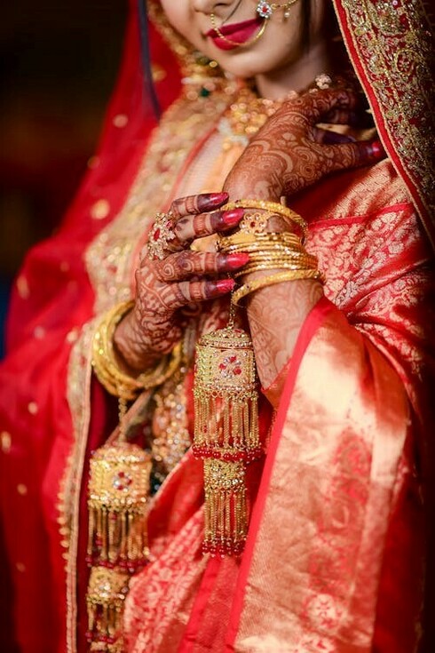 The beauty of Kumaoni weddings shines through a bride in red, complemented by elegant golden bracelets that symbolize tradition and joy