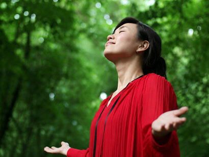 A woman closes her eyes and listens to the sounds of birds while enjoying the tranquility of the forest