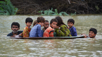 Un par de adultos ayudan a un grupo de niños a cruzar un camino tras las fuertes inundaciones en Pakistán, 2022