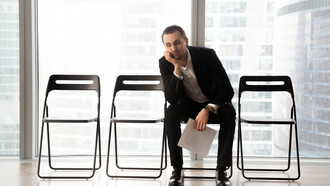 A bored young man in a suit sits in a waiting room for a job interview, looking upset