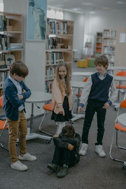 A young boy is being bullied by his classmates and cowers on the ground