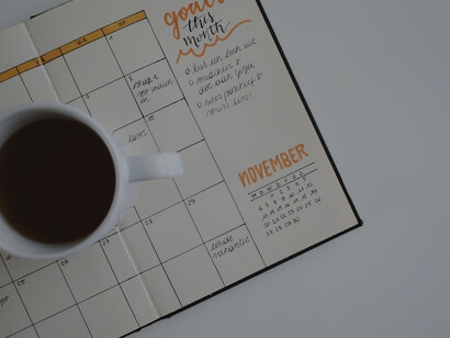 A white ceramic mug filled with coffee resting atop an open planner