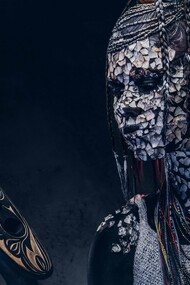 A person from an indigenous African tribe wearing traditional makeup and costume while staring at a mask in their hand, symbolizing the struggle of the modern African youth caught between tradition and modernity