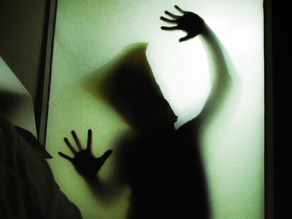 La silueta de una persona aparece detrás de una superficie iluminada, con las manos apoyadas y levantadas hacia la luz