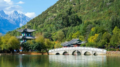 A historic stone bridge leading toward classical pavilions at Jade Dragon Snow Mountain, China, symbolizing the harmony between centuries-old traditions and contemporary development