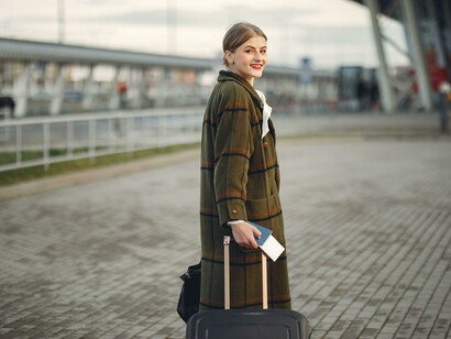 A stylish woman walking near a contemporary building with luggage, passport, and boarding ticket