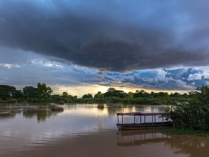 Nubes azules y tormentosas al atardecer, con reflejos en el agua y una piragua amarrada a la orilla, en Don Det, Laos