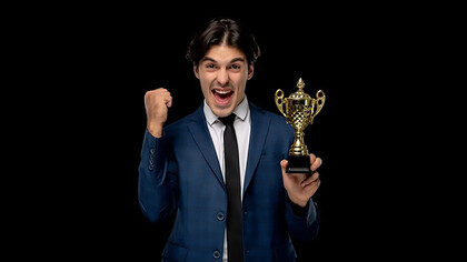 Successful young businessman in a dark blue suit and tie, holding a trophy with excitement