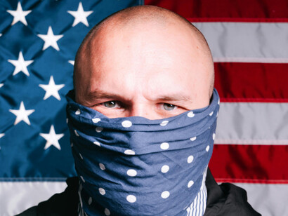 A man covering his face with an American flag behind him