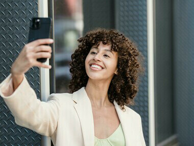 A smiling woman takes a selfie with her smartphone in the city, capturing a candid urban moment