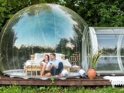 Glamping experience with a couple in a transparent bubble tent, complemented by geodesic domes in a sustainable hotel setting
