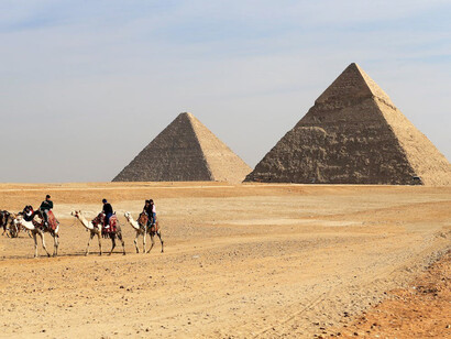 Four individuals riding camels in front of the iconic pyramids of Giza, Egypt