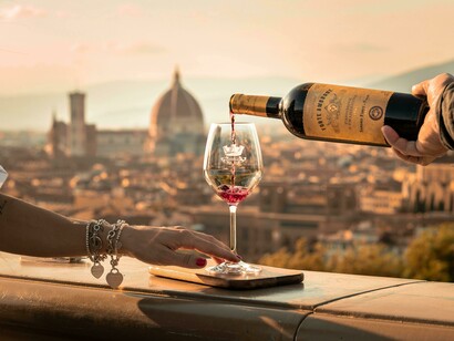 The hands of a couple, gracefully holding wine glasses, share a quiet moment in a beautiful town in Tuscany