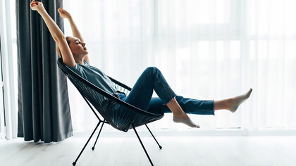 A young woman relaxes in her modern living room, sitting on a stylish chair by the window, embodying the essence of minimalist living