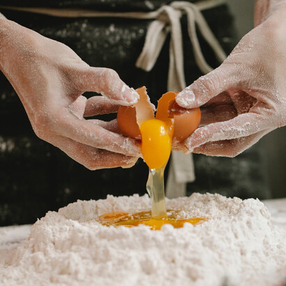 Aprendiz de cozinha quebra ovo em cima de uma massa de farinha