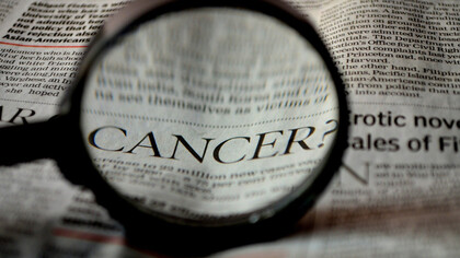 Beneath the magnifying glass, the word 'cancer' becomes apparent on the newspaper