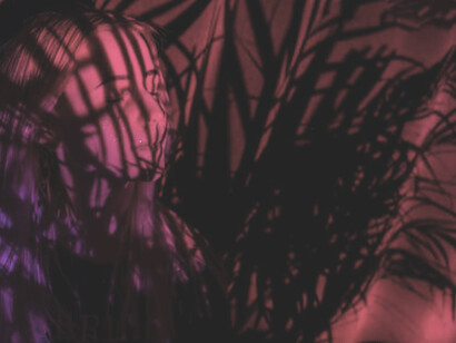 Beneath the dappled shadows of palm leaves, a woman stands bathed in the warm, crimson glow of red light