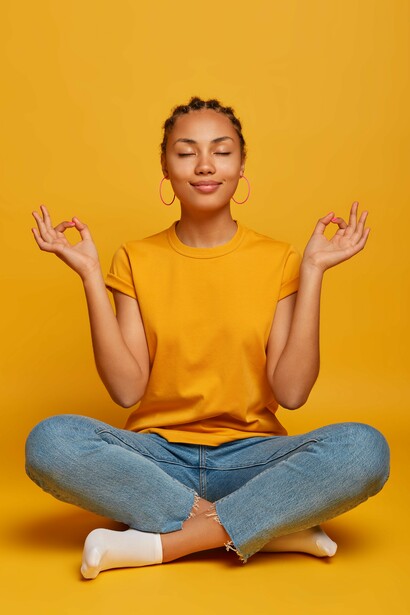 A woman looking peaceful as she sits with crossed legs on the floor, practicing yoga and trying to relax with her eyes closed