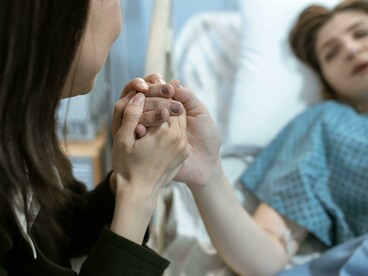 Hospital visitor clasping a patient’s hand in a caring and emotionally supportive gesture