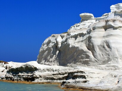 Stark volcanic cliffs contrasting with vivid blue sky, symbolizing the striking natural palette that has earned Milos its reputation as the island of colors