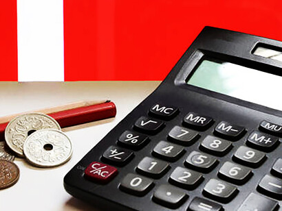 A neat stack of Danish coins, paired with a vibrant red wooden pen, rests on a pristine white backdrop, while a calculator sits elegantly against the backdrop of the Danish national flag