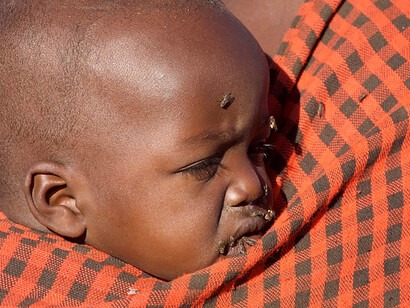 A vulnerable infant finds comfort in the embrace of his mother, their poignant reality marred by the presence of flies on his face, Maasai, Tanzania