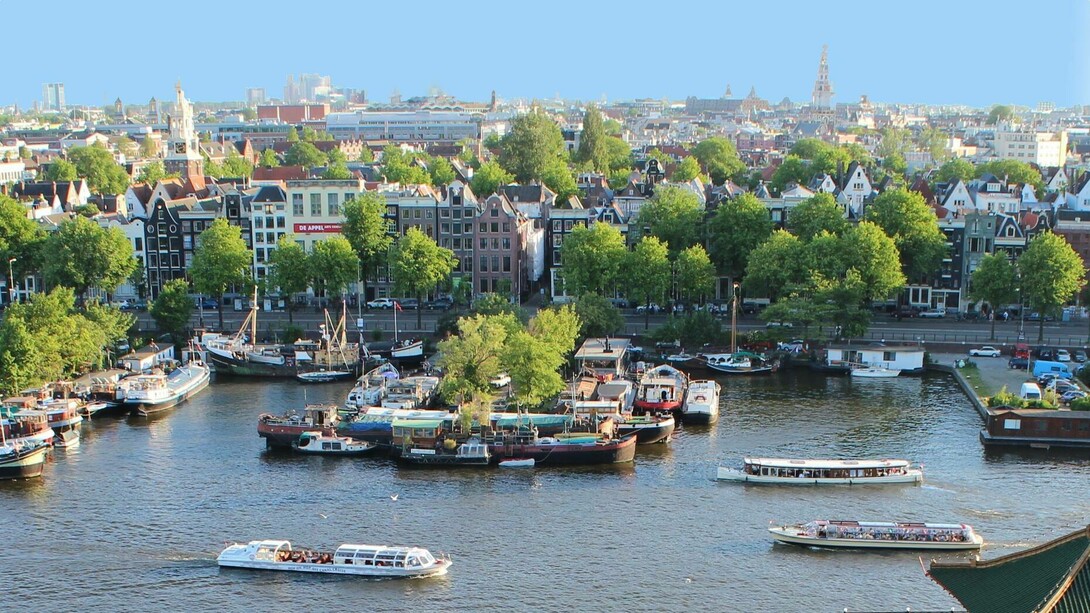 Vista de Amsterdã, Holanda. Ela ligou o motor. O barco, lento como o meu olhar, atravessava pequenas ondinhas formadas pelo vento e pelo balançar do barquinho