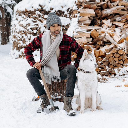 A man and his dog sitting quietly by a pile of firewood in a snowy landscape