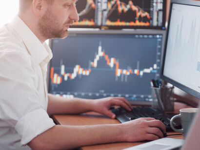 In a trading room, a stockbroker in a shirt reviews display screens, tracking stock market fluctuations, forex, and financial graphs, as economic instability and risks threaten the US market