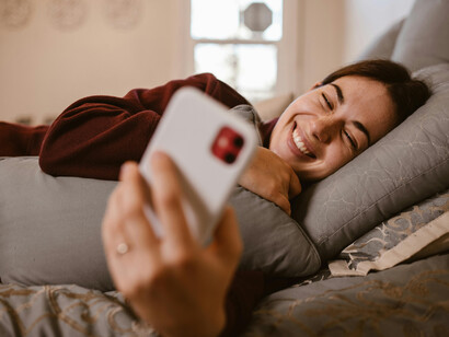 A woman rests in bed, her eyes filled with emotion as she talks to her boyfriend over the phone in their long distance relationship