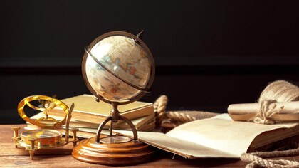 A globe and compass placed on books on a table, symbolizing the need for global citizenship, education, and the guiding wisdom of philosophy