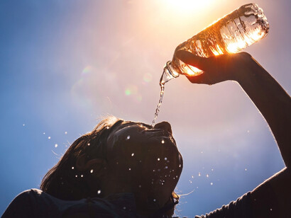 A woman cools herself by splashing water on her face during a hot summer day