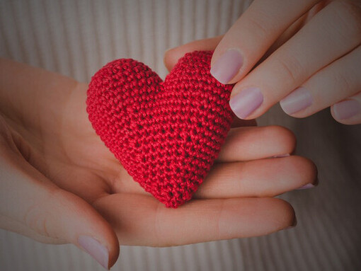 A close-up of hands delicately cradling a knitted heart, embodying love and tenderness