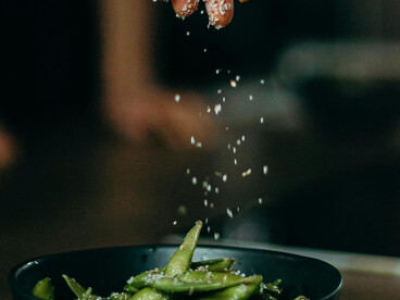 A close-up of sweet peas being stir-fried and salt poured over green beans, highlighting nutritious vegan snacks