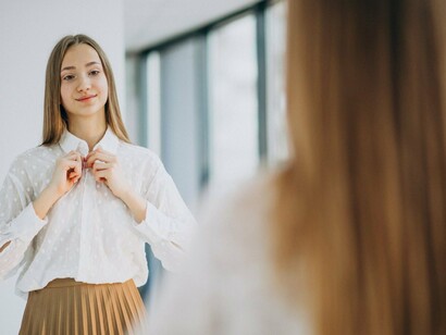 A woman meeting her own eyes with a gentle smile, reflecting a nurturing and compassionate inner voice
