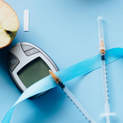 Media manzana roja, medidor de glucosa en sangre, jeringas y agujas, y lazo celeste