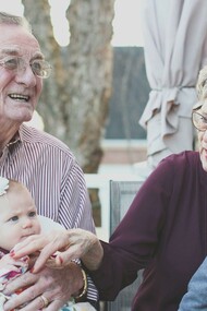 An elderly grandmother and grandfather lovingly hold their grandchild on their lap
