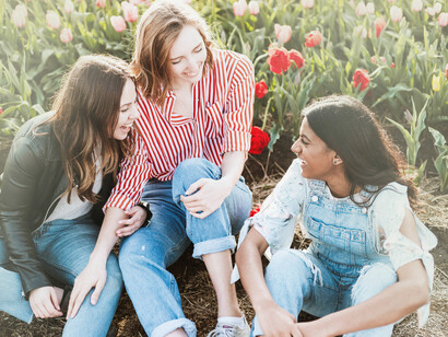 A trio of friends, one from different ethnicity, sharing a laugh and smiles in a field of roses which makes us feel like the world is in decent hands