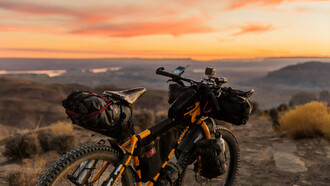 An orange and black off-road bicycle perched on a hill during sunset, with the warm glow of the fading light illuminating the scene