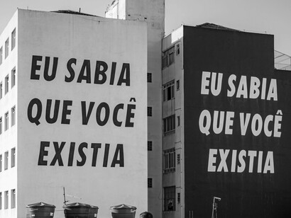 Em preto e branco, o mural revela o contraste entre forma e sentido, reafirmando a força simbólica das palavras. A linguagem escrita, seja no livro ou na cidade, tem o poder de tocar e permanecer