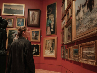A visitor exploring a gallery with historical paintings on dark red walls, highlighted by low light, demonstrating art gallery illumination and exhibition space lighting techniques