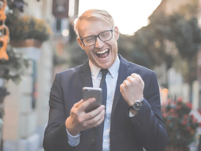 A well-dressed gentleman, sauntering along the road, exudes delight upon receiving favorable news during a phone call