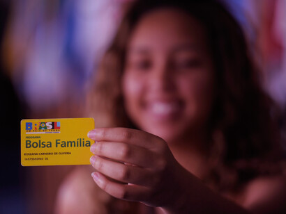 A young woman beams with pride as she holds her Bolsa Família card, a symbol of the financial support that has transformed lives across Brazil by addressing basic needs and reducing poverty