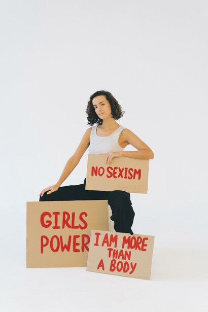 Uma mulher mostrando três cartazes 'Sexismo não', 'Poder feminino' e 'Eu sou mais do que um corpo'