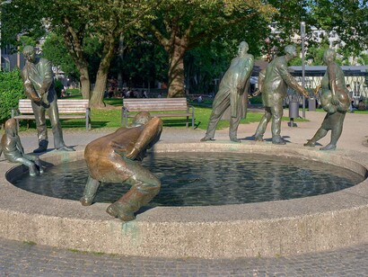 Las distintas figuras de la fuente representan el ciclo del dinero, del que toma su nombre, y sus acciones giran en torno a él . Representan la avaricia , la codicia , el clientelismo y la mendicidad. Se muestra a un niño observando a su padre contar dinero. Karl-Henning Seemann,1976. "Ciclo del Dinero" Aquistrán, Alemania