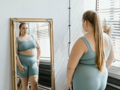 A woman studying her silhouette in the mirror, symbolizing the challenge of adapting to a body that no longer fits familiar proportions